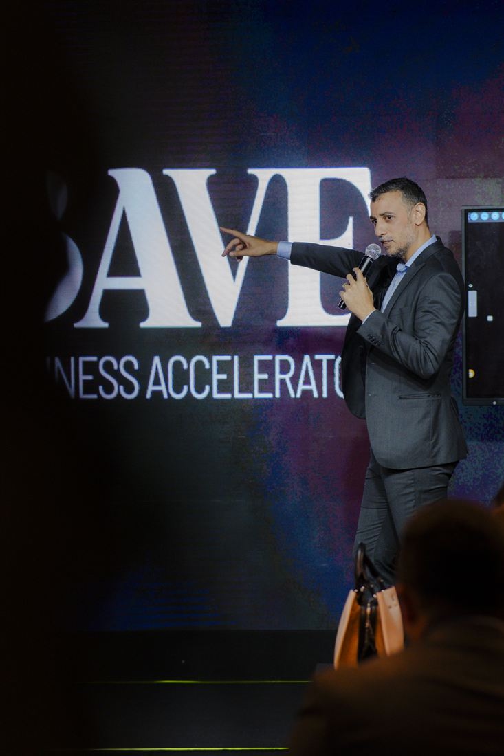 Marcos Araújo no palco do BAVE Business Accelerator, microfone na mão, apontando para a plateia